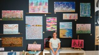 Die Künstlerin steht in einem großen Raum vor Ihren Bildern.