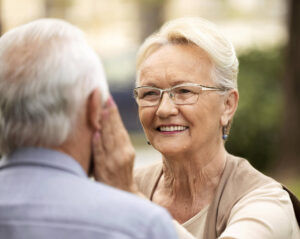 Eine Seniorin legt einem Senior liebevoll eine Hand an die Wange und lächelt. Symbolbild für Leistungen aus der Pflegeversicherung Bremen für pflegende Angehörige
