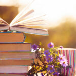 Bücherstapel neben einer bunten Tasse und lila Blümchen