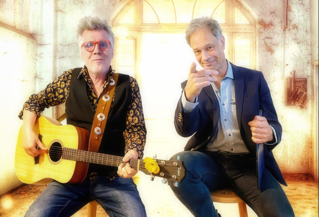 Der Gitarrist Jürgen Schöffel (links) mit Akustikgitarre und der Sprecher Martin Heckmann (rechts) sitzen auf Hockern vor einem hellen Hintergrund und präsentieren gemeinsam das Lesungsformat „Blumenthaler Geschichten“.