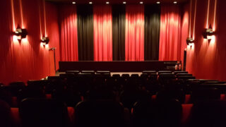 Blick in einen leeren Kinsosaal mit rot-schwarzem Vorhang vor der Leinwand