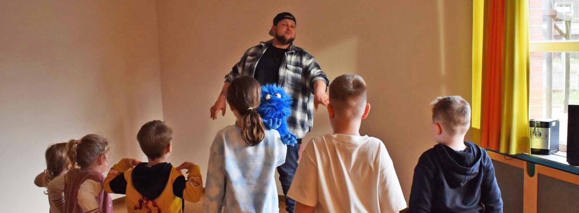 Gruppe von Kindern steht in einem Raum und macht gemeinsam Bewegungsübungen mit einem Trainer