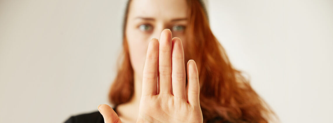 Junge Frau mit erhobener Handfläche in Stop-Geste blickt selbstbewusst nach vorn – Symbolbild für Selbstbehauptung, klare Grenzen und sicheres Auftreten im Alltag.