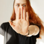 Junge Frau mit erhobener Handfläche in Stop-Geste blickt selbstbewusst nach vorn – Symbolbild für Selbstbehauptung, klare Grenzen und sicheres Auftreten im Alltag.