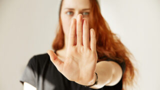 Junge Frau mit erhobener Handfläche in Stop-Geste blickt selbstbewusst nach vorn – Symbolbild für Selbstbehauptung, klare Grenzen und sicheres Auftreten im Alltag.