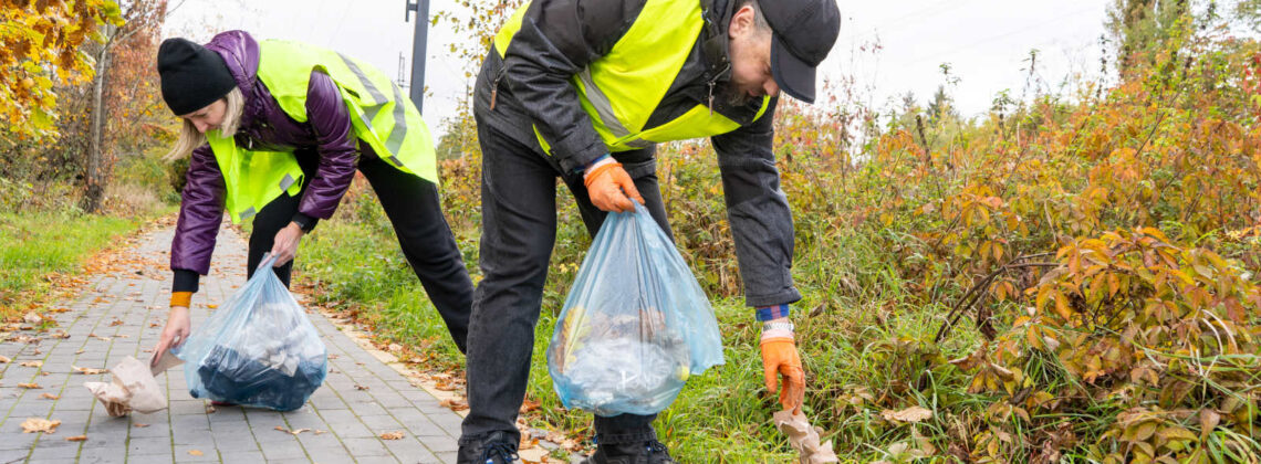 Zwei Menschen in Warnwesten bücken sich und sammeln Müll auf