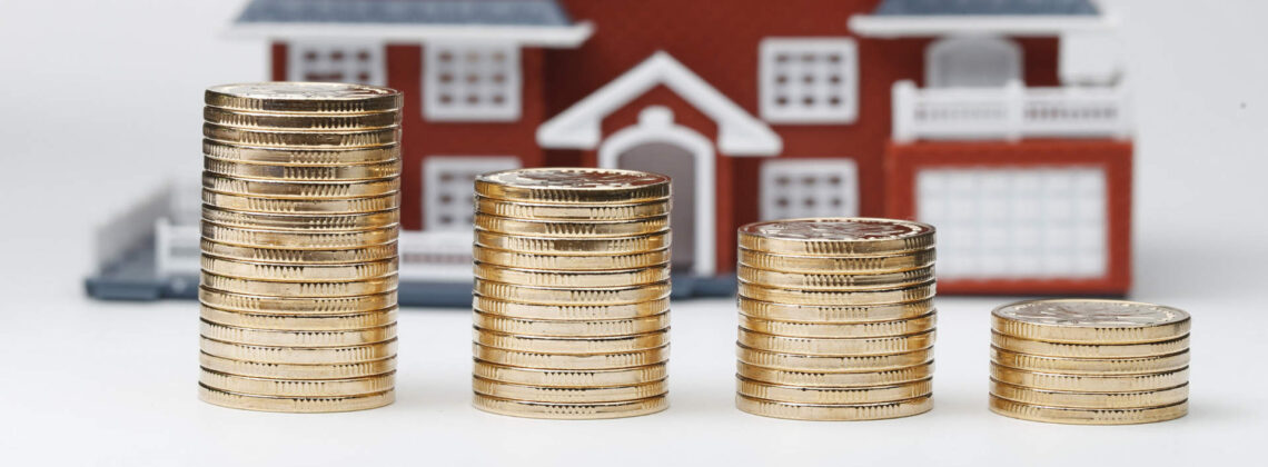 Drei kleiner werdende Stapel Münzen liegen vor einem Modellhaus - Symbolbild für Eigenkapitel für Immobilien Bremen