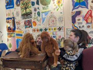 Ein Mann erzählt mit Orang-Utan-Handpuppen einer Frau und einem Kind Geschichten im k:ulaBi