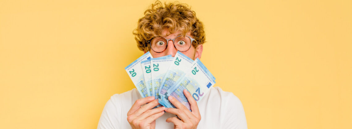 Junger Mann hält gefächerte 20-Euro-Gelscheine vor sein Gesicht