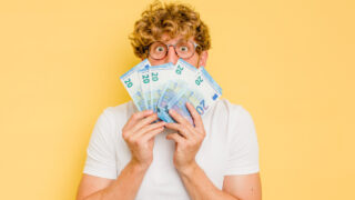 Junger Mann hält gefächerte 20-Euro-Gelscheine vor sein Gesicht