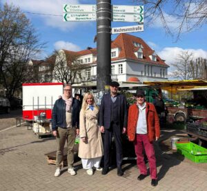 Vier Vorstandsmitglieder des Vereins Die Wachmannstraße stehen gemeinsam auf dem Benqueplatz in Bremen