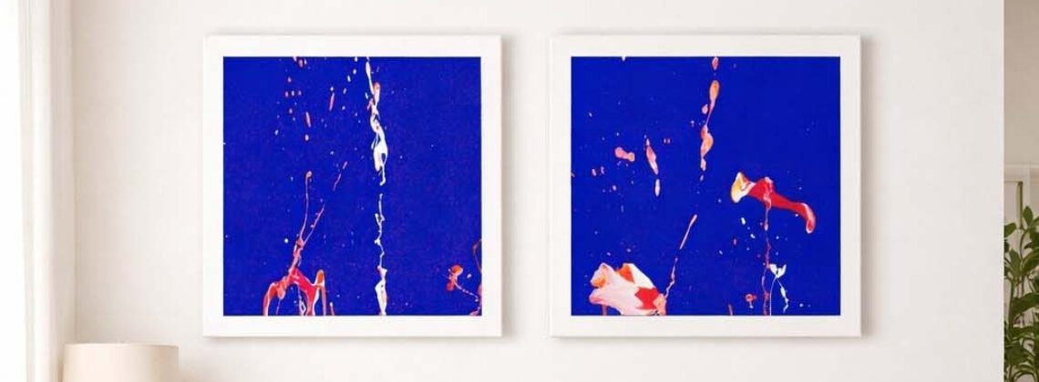 Zwei abstrakte Bilder mit blauem Hintergrund und farbigen Farbbewegungen hängen über einem Sofa.