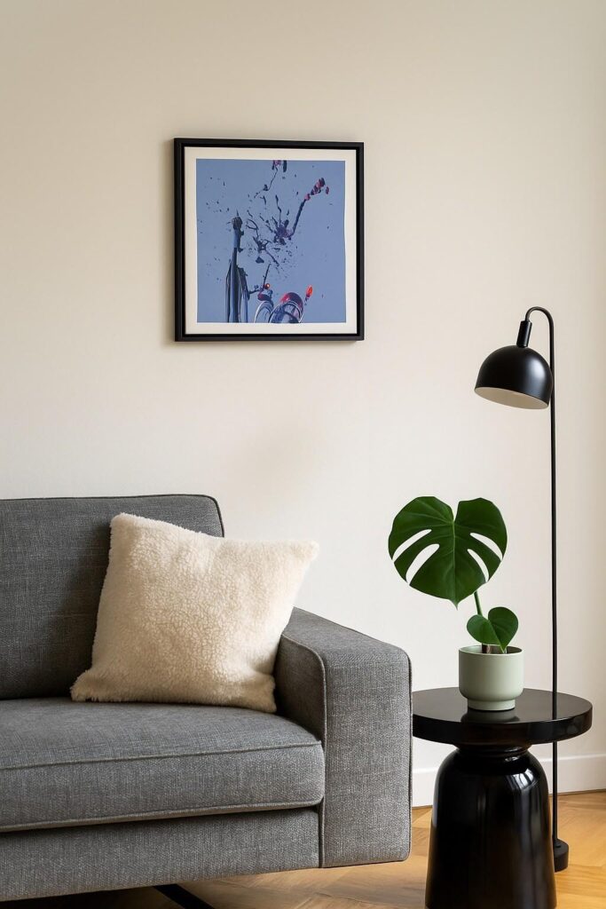 Kleines gerahmtes abstraktes Bild mit blau-grauem Hintergrund und feinen Farbspritzern über einem Sofa.