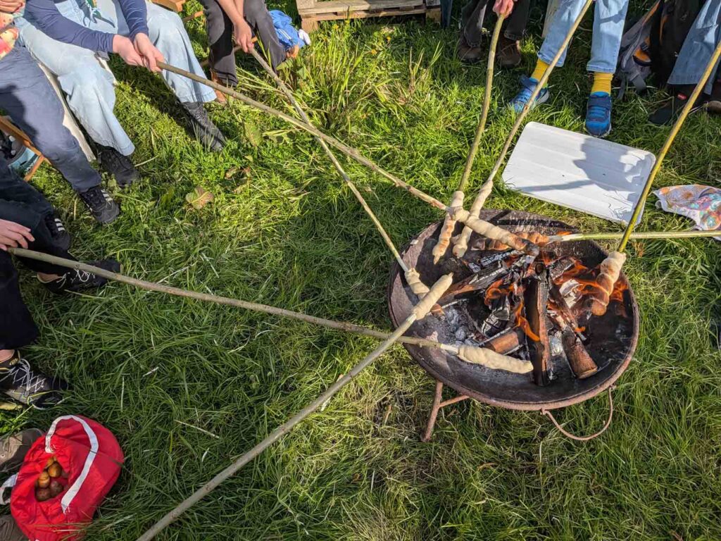 Kinder und Erwachsene backen Stockbrot über einem Lagerfeuer im Klimagarten Findorff