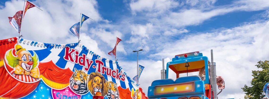 Bunter Kinder-Truck fährt auf einer Schiene neben einem Zirkusmotiv.