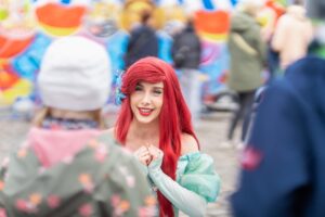 Frau im Meerjungfrauenkostüm spricht mit Kindern auf einem Festplatz.