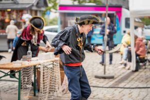 Zwei Personen in Piratenkostümen spielen eine Szene auf einem Festplatz.
