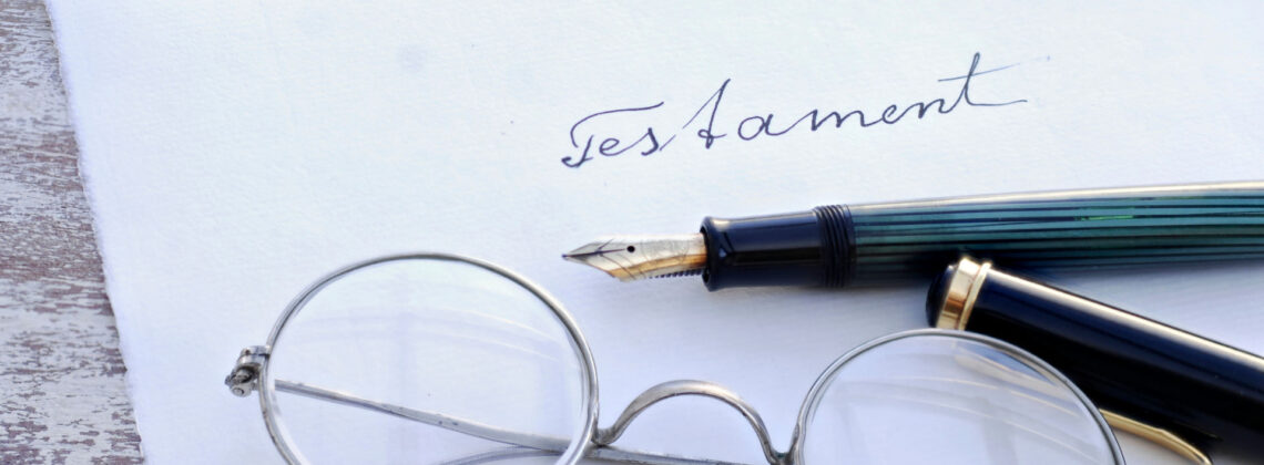 Auf einem Bogen Papier liegt ein Stift und eine Brille. Afu dem Papier steht: Testament.