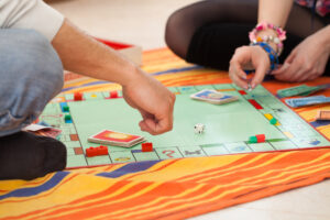 Zwei Personen spielen gemeinsam ein Brettspiel auf einer orange gestreiften Decke.