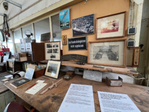 Ausstellungstisch im Dat lütje Museum Blumenthal mit historischen Fotos, Schildern, Mess- und Arbeitsgeräten sowie Dokumenten zur Bremer Woll-Kämmerei und zum Heizkraftwerk.