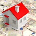 Das Foto zeigt ein Modellhaus mit rotem Dach, das auf einem Haufen 50 Euro Scheine steht. Symbolbild für: Finanzierung Immobilien Bremen
