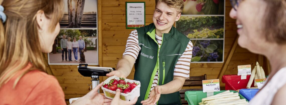 Hofläden Bremen: ein junger Mann von Alfkens Hof überreicht eine Schale Erdbeeren
