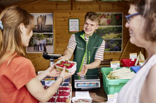 Hofläden Bremen: ein junger Mann von Alfkens Hof überreicht eine Schale Erdbeeren