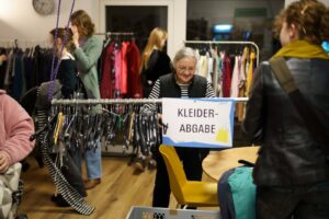 Menschen stöbern bei einer Kleidertauschbörse im Quartierstreff Jetzt Hier zwischen Kleiderständern.
