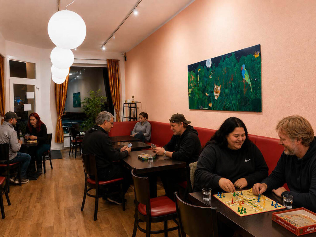 Menschen sitzen abends im Bremer Nachtcafé zusammen, spielen Gesellschaftsspiele und kommen an mehreren Tischen miteinander ins Gespräch.