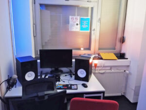 Ein Arbeitsplatz mit Monitor, Studiolautsprechern und Mikrofon in einem kleinen Tonstudio.