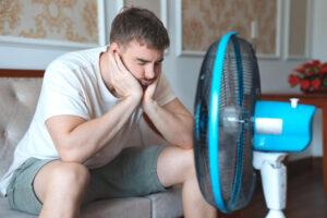 Mann sitzt bei Hitze vor einem Ventilator in der Wohnung