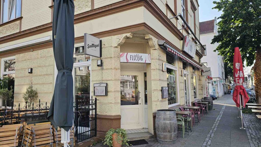 Eckgebäude des Bar-Restaurants Flüssig an der Pappelstraße in Bremen mit Außenplätzen, Weinfass und Sonnenschirm