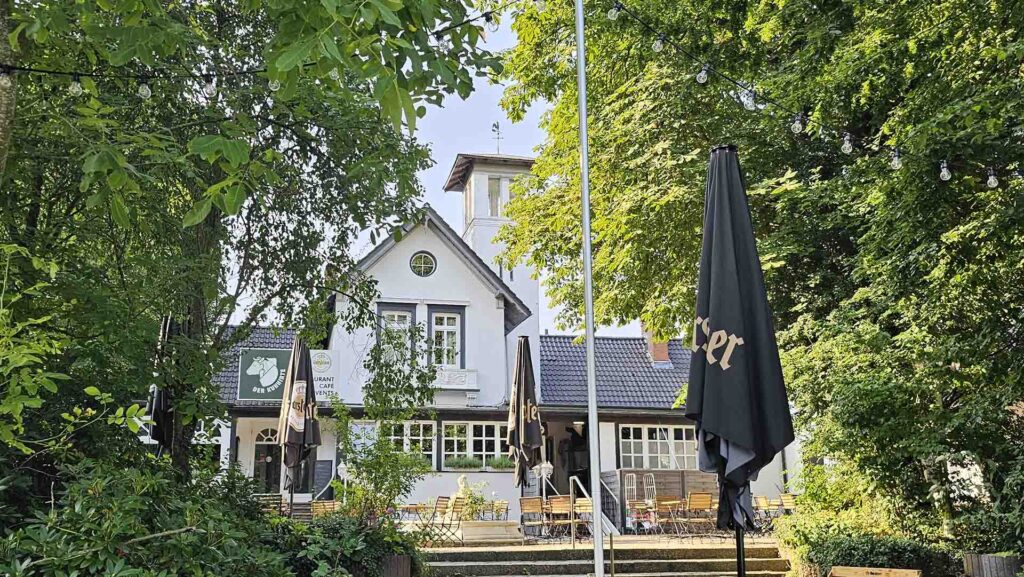 Historisches weißes Gebäude des Traditonsrestaurants Der Kuhhirte am Werdersee, umgeben von grünen Bäumen