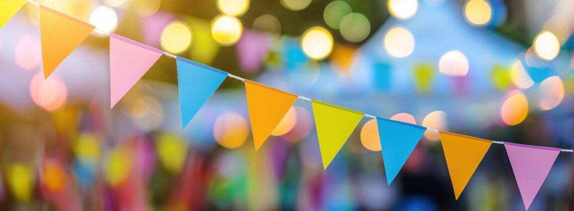 Girlande mit bunten Dreiecksfahnen, im Hintergrund ein Stadtteilfest