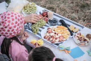 Zwei Kinder sitzen an einem Picknicktisch, auf dem kleingeschnittenes Obst in Hülle ud Fülle liegt