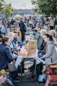 Menschen sitzen an reich gedeckten Picknicktischen und unterhalten sich