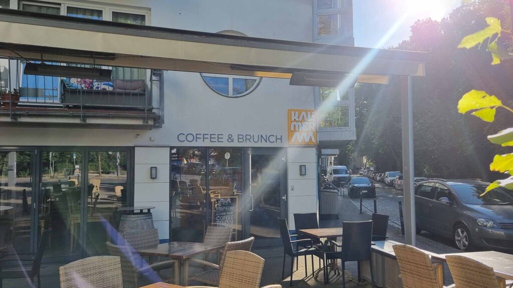 Außenansicht von Kalimeraaa mit Tischen und Stühlen sowie einfallenden Sonnenstrahlen
