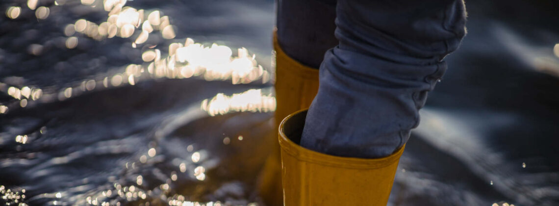 Nahaufnahme auf gelbe Gummistiefel in knöchelhohem Wasser, Symbolbild für Schutz vor Starkregen