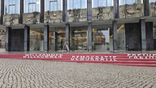 Fassade der Bremischen Bürgerschaft mit roten Stufen und den Schriftzügen „Willkommen“, „Demokratie“ und „Freiheit“.