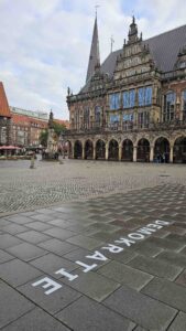 Bremer Rathaus am Marktplatz mit dem Schriftzug „Demokratie“ auf dem Pflaster im Vordergrund.
