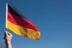 Eine Hand hält eine Deutschlandflagge vor blauem Himmel.
