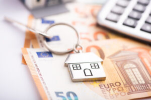 Ein Schlüssel mit einem kleinen Häuschen als Anhänger liegt auf 50 Euro Scheinen neben einem Taschenrechner, Symbolbild für Finanzierungsmodelle Immobilien Bremen