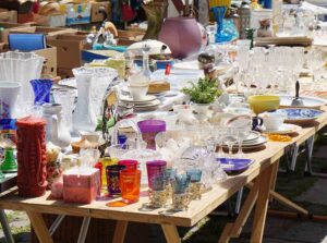 Ein Flohmarkttisch mit zahlreichen bunten Gläsern, Vasen, Tassen, Tellern und weiteren gebrauchten Haushaltsgegenständen.