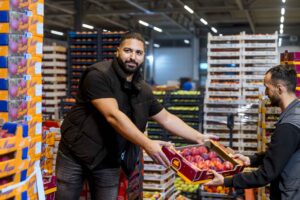 Zwei Händler übergeben auf dem Großmarkt eine Kiste mit frischem Obst