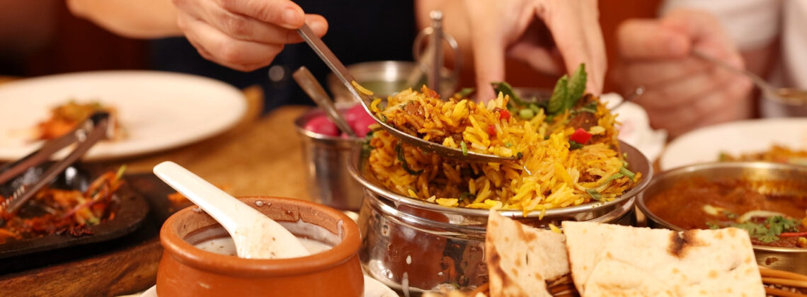 Restaurants in Findorff: Hände servieren traditionellen indischen Biryani-Reis mit Naan und Curry