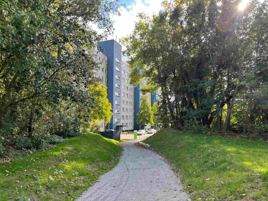 Ein Weg vom Klimapark Oslebshausen führt zur Wohnanlage Wohlers Eichen, von der man ein Hochhaus sieht.